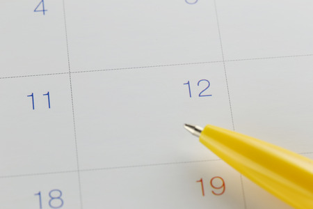 yellow pen points to the number 12 on calendar background in concept of appointment schedules and important dates.の写真素材