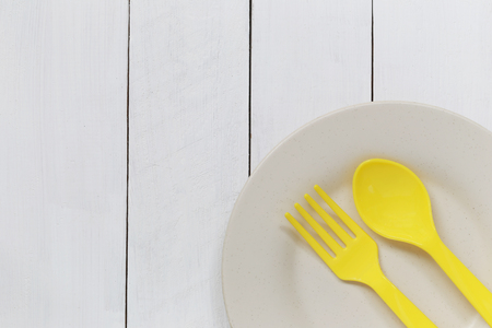 Plate and yellow plastic spoon placed on white wood background and have copy space for design in your work.の写真素材