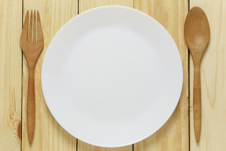 White plate and wooden spoon rests on a brown wood floor and has copy space for your design ideas.の写真素材