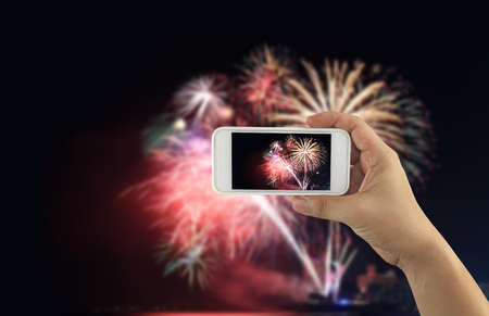 hand of a businessman holding a smartphone to take a pictures at night and fireworks on dark sky for design idea in your work.の写真素材