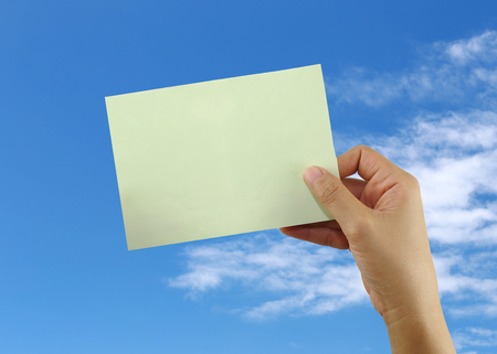 hand of a businessman holding a blank green note paper on blue sky background.の写真素材
