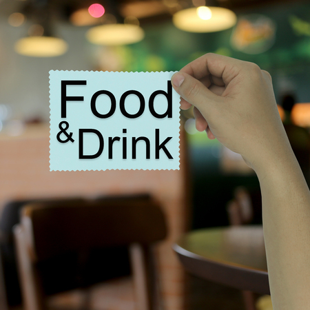 Hand of the businessman holding a paper note and have Food & drink text on blur restaurant background for design in your work.の写真素材