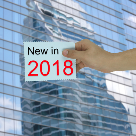 Hand of the businessman holding a paper note with new in 2018 text on high buildings background for...