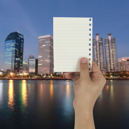 Hand of the businessman holding a empty paper note on twilight city background in concept of profitability in doing business for design in your work.の写真素材