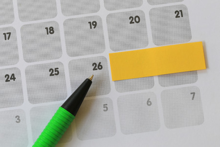 Green pen points to a twenty six number of calendar and have blank yellow note paper for design concept of important day in you work.の写真素材