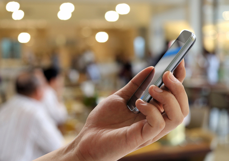 Hand of man holds a smartphone on blur restaurant background and have copy space for design present in your work concept.の写真素材
