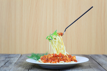 Spaghetti with tomato sauce on silver fork of floating in the white dish on wooden floor,concept of eating good food is health care.の写真素材