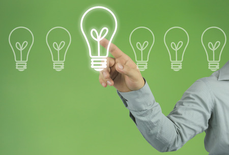 Hand of businessman pointing to a light bulb in the concept of design and ideas on green background.の写真素材