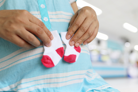 Pregnant mothers holding a small pair of socks on stomach for design in your work about pregnancy concept.の写真素材
