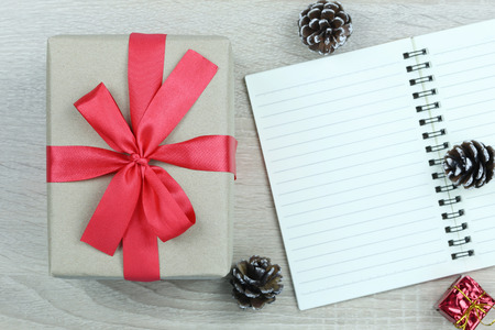 Brown gift box with red bow on wooden floor and blank book in Christmas and new year concept for your design.の写真素材