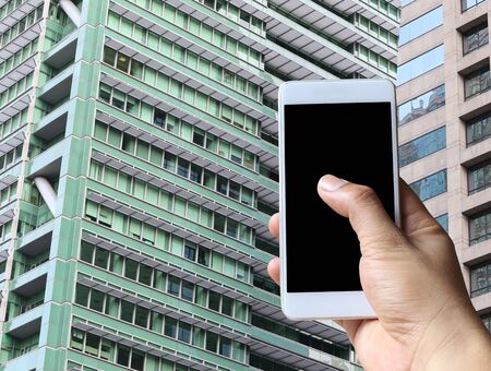 Hand of a man holding a blank smartphone device on the Skyscraper background.の写真素材