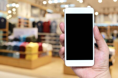 Hand of a man holding smartphone device in the blur Shopping mall background and have white copy space on screen.の写真素材