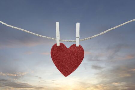 Red heart hanging on a hemp rope on the morning sky background for design in your work concept.