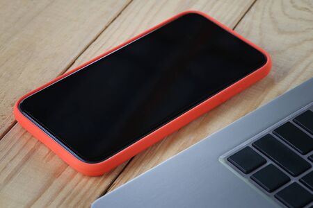 Blank screen of smartphone and a laptop placed on a wooden desk and have copy space for design in...