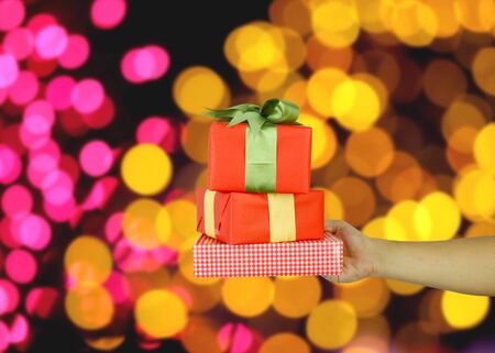 Hand of man with a red gift box on bokeh background for design in your work concept.の写真素材