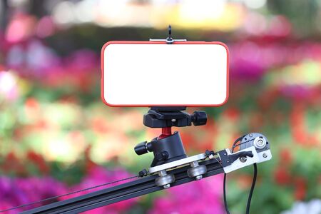 Smartphone with a blank screen on the slide rail,On the background of a colorful, blurred flower garden.の写真素材
