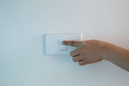 Woman's hand is turning off the light switch on wall,Concept of energy saving.