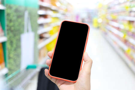 Hand is holding the smartphone and has a blank black screen in the shopping mall.