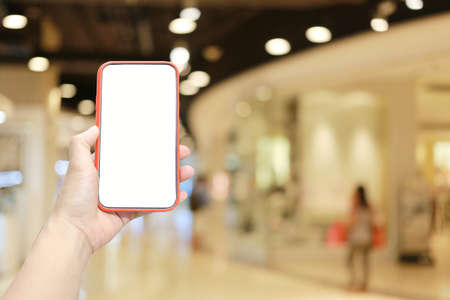 Hand of a man holding smartphone device in the Shopping mall background and have white copy space on...