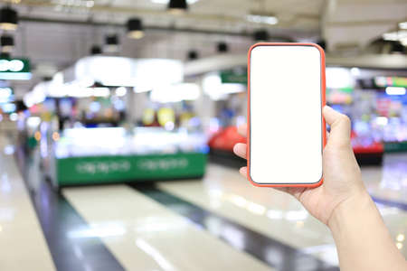 Hand of a man holding smartphone device in the Shopping mall background and have white copy space on...