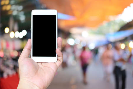 Hand of a man holding smartphone device in the Shopping market background and have white copy space...
