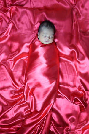 Asian baby boy sleeping comfortably in red cloth,newborn baby cuteness.の写真素材