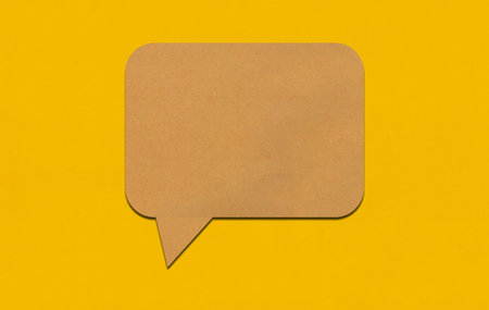 Brown paper speech bubble on yellow paper background. Paper blank of text box with copy space for advertisement design.の写真素材