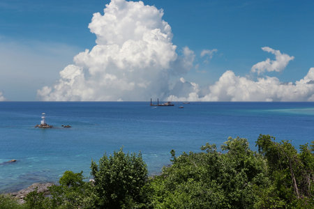 Blue sea with boats floating on the surface on a clear day. There are mountains and trees.