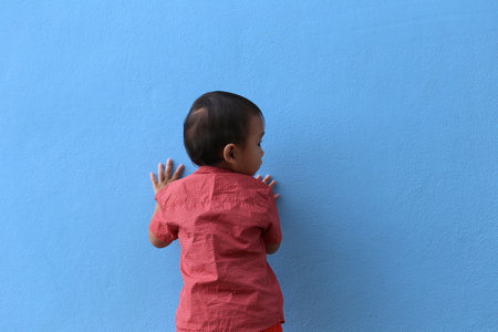 An Asian boy in a red shirt turn your back is standing against a blue wall.の写真素材