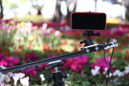 A smartphone with a blank black screen mounted on a dolly slider was used to film a video with a blurred background of a flower garden.の写真素材