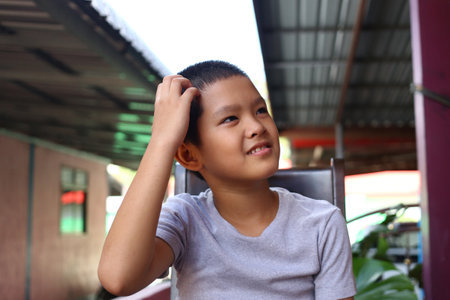 A young boy sits thoughtfully, exhibiting a range of emotions with a smile. His casual attire reflects a relaxed moment of contemplation in an indoor setting.の写真素材