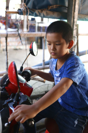 A young boy engages in play on a vibrant red toy motorcycle, captured in an outdoor setting. The scene reflects joy, imagination, and childhood adventure.の写真素材
