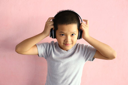 A cheerful boy wearing headphones smiles while listening to music indoors. His playful expression...