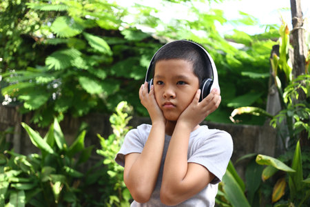 A young child wearing headphones enjoys music while surrounded by lush greenery. The image captures the joy and serenity of outdoor music listening.の写真素材