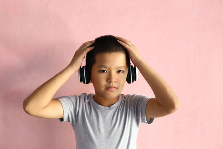 A young boy expresses joy while listening to music with headphones in a casual indoor setting. The pink background adds a playful touch to the moment.の写真素材