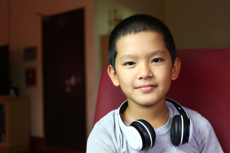 A young boy smiles confidently while wearing headphones in a cozy indoor environment. This portrait captures the joy and innocence of childhood, showcasing a moment of relaxation and connection to music.の写真素材
