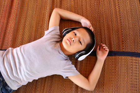 A relaxed boy lying on a woven surface, wearing headphones and immersed in music. His serene...
