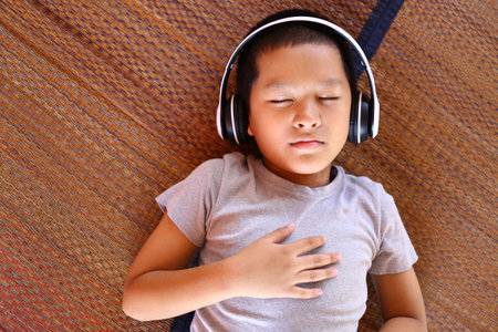 A young boy enjoys a moment of relaxation while listening to music with headphones. The scene...