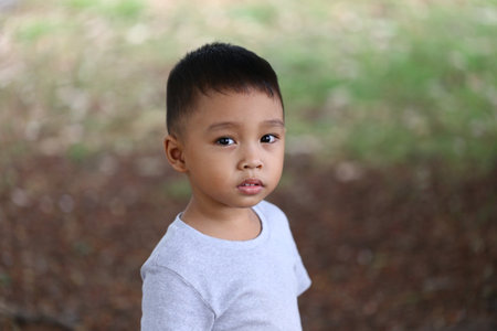 A young boy stands outdoors, gazing thoughtfully into the distance. His serious expression and casual attire highlight the innocence of childhood in a natural setting.の写真素材