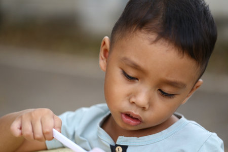 A close-up view of a focused young boy engaged in a playful activity. His expression of curiosity and innocence captures the joy of childhood exploration and discovery.の写真素材