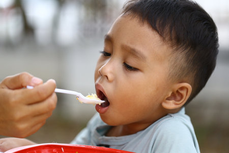 A young boy enjoys a meal while being lovingly fed by a parent. The image captures the joy and connection during mealtime, showcasing care and happiness.