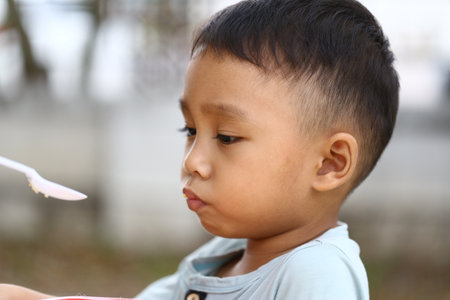 A thoughtful young boy enjoys his meal outdoors, capturing a moment of innocence and joy. This portrait reflects the carefree spirit of childhood in a natural setting.の写真素材