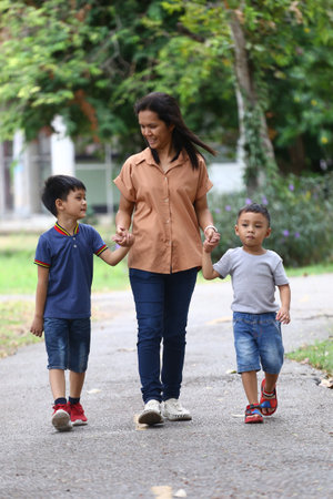 A joyful family moment captured in a park as a mother walks hand in hand with her two young children, enjoying quality time and nature.の写真素材