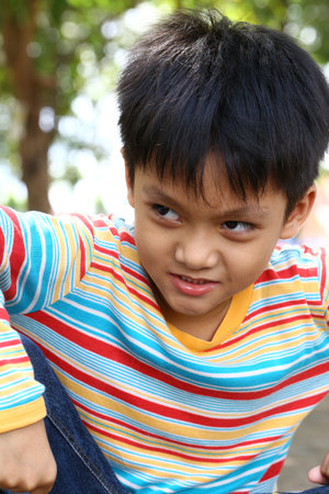 A joyful boy poses outdoors in a colorful striped shirt, showcasing a playful expression. Surrounded by nature, he embodies youth and happiness.の写真素材