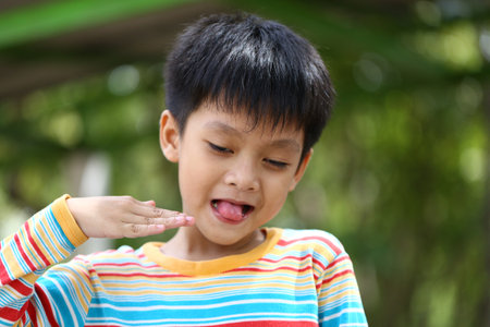 A joyful boy playfully sticking out his tongue with a cheerful expression. Captured in a vibrant outdoor setting, showcasing innocence and fun.の写真素材