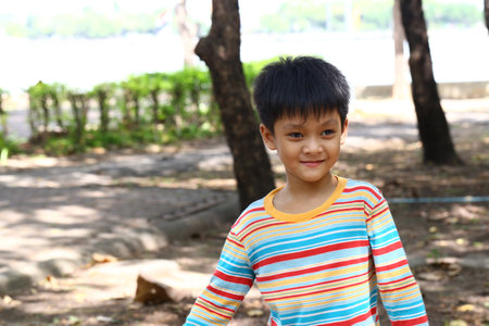 A joyful young boy in a vibrant striped shirt enjoys playing outdoors, surrounded by nature and...