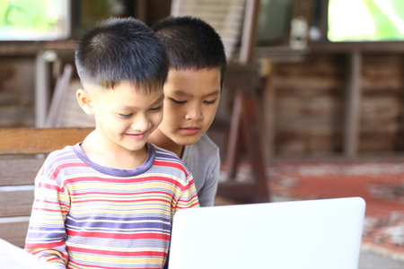 Two young boys are happily interacting with a laptop, showcasing the joy of technology and learning. Their cheerful expressions reflect a moment of discovery and friendship.の写真素材