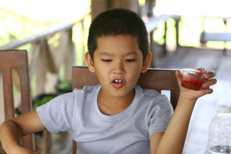 A young boy holds a snack jar while sitting outside in a rustic setting. His cheerful expression captures the joy of childhood and simple pleasures.の写真素材