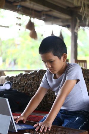 A young boy sits indoors, focused on his laptop, engaged in a digital task. The serene environment highlights his concentration and creativity.の写真素材