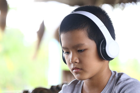 A young boy wearing white headphones enjoys listening to music in a serene indoor setting,...